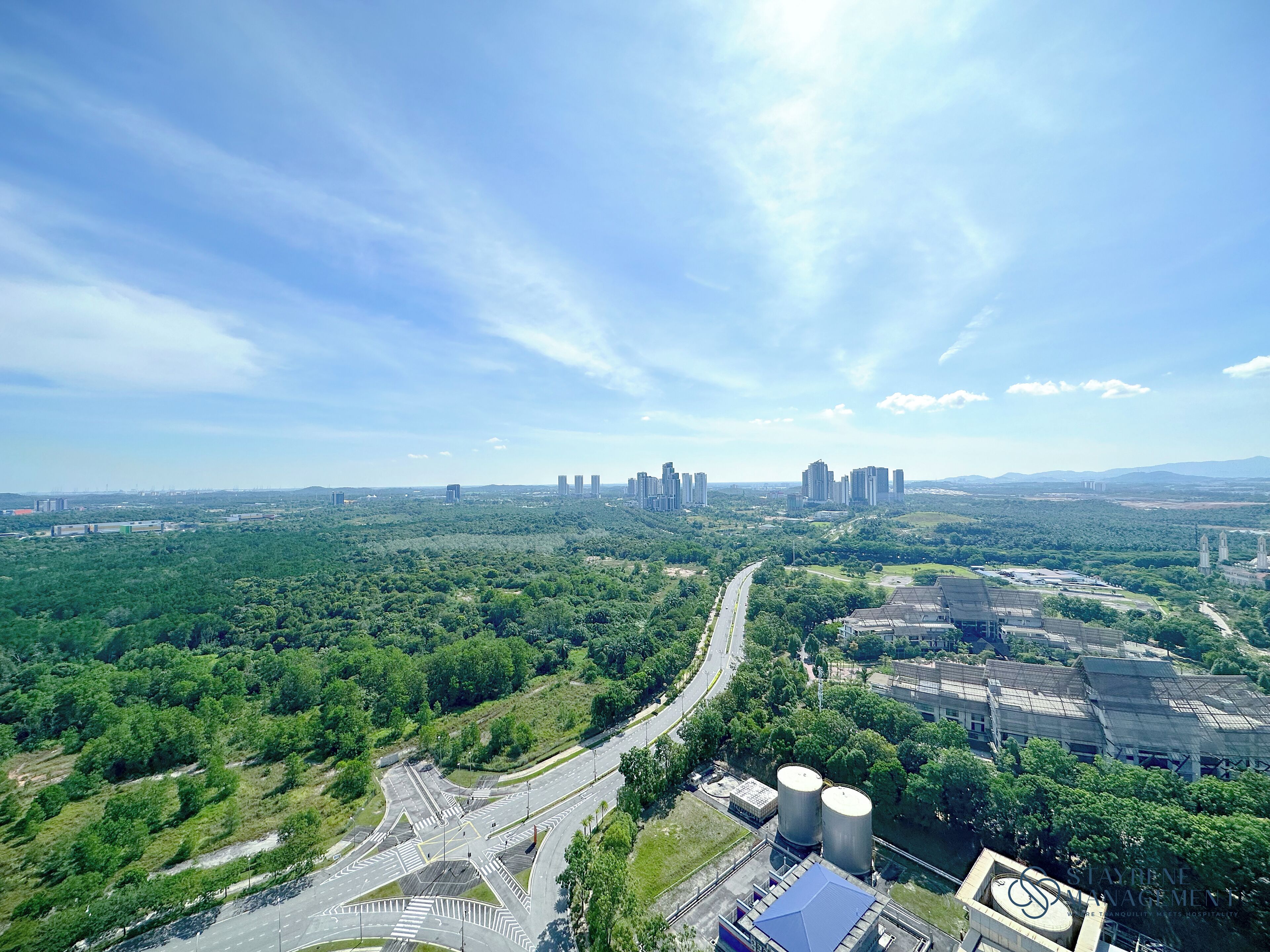 An aerial view of a city with a mix of green spaces and urban development, including a highway and industrial buildings.