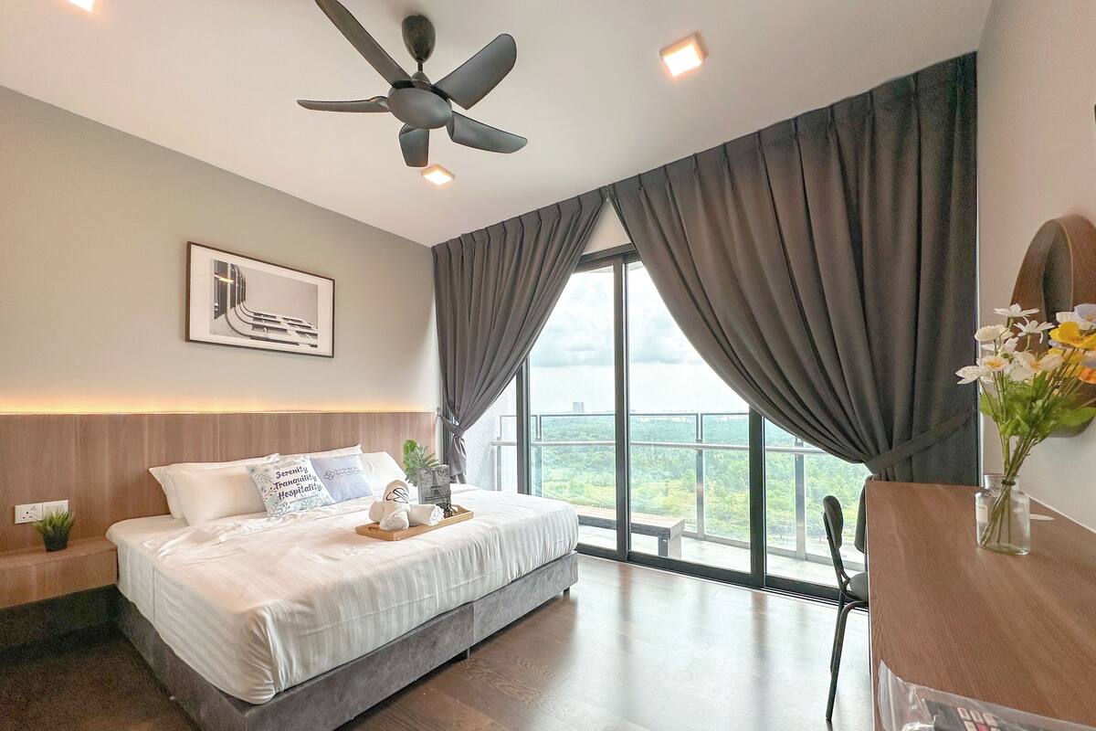 Una habitación de hotel moderna con una cama grande, ventilador de techo, vista al exterior y un escritorio con un jarrón de flores.