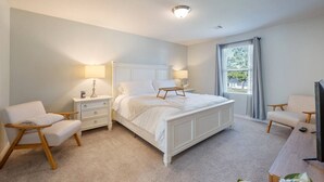 A bedroom with a large bed, two bedside tables, a nightstand, a TV, and a window with curtains.