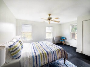 Un dormitorio con cama, ventilador de techo, radiador y ventana.