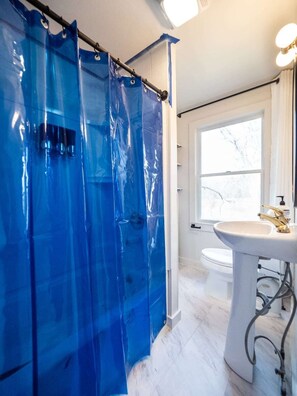 Un baño con lavamanos blanco, ventana y cortinas de ducha azules.