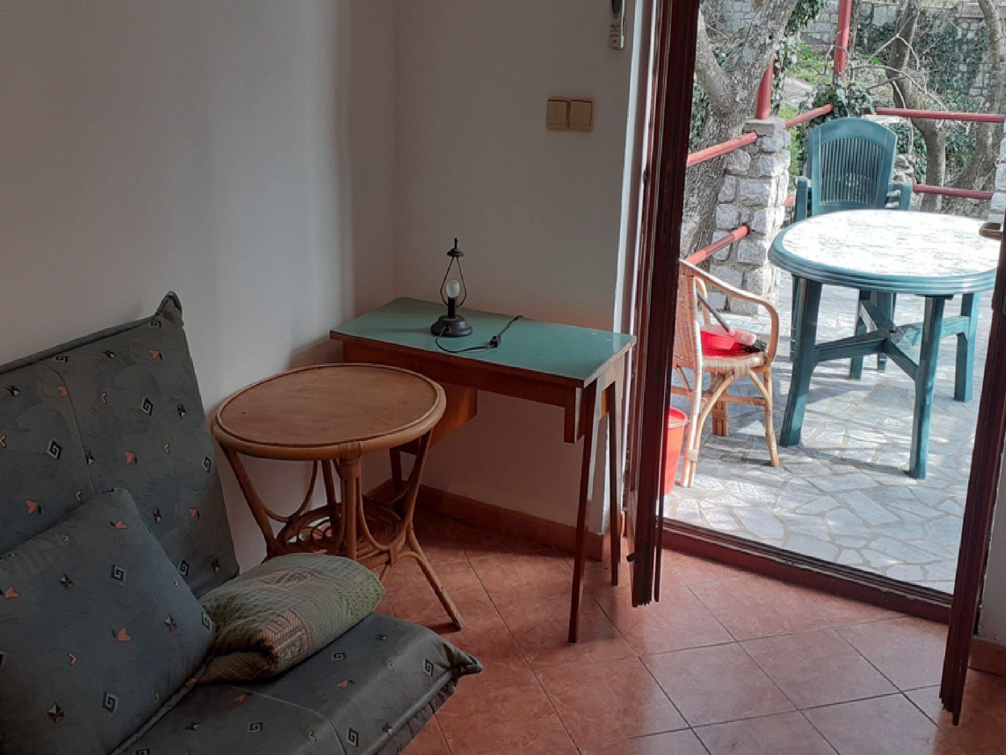 A room with a sofa, a small table, and a chair. There is a window with a view of an outdoor area.