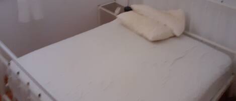 A white bed with a white pillow in a room with white walls and a white headboard.