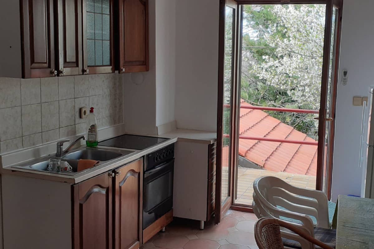 A kitchen with wooden cabinets, a dishwasher, and a sliding glass door leading to a balcony with a red roof.
