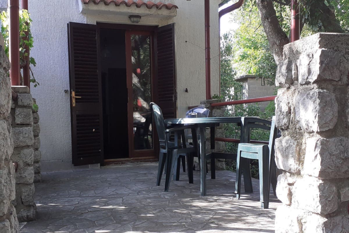 A stone-floored patio with a table and chairs, a door with shutters, and a stone wall.