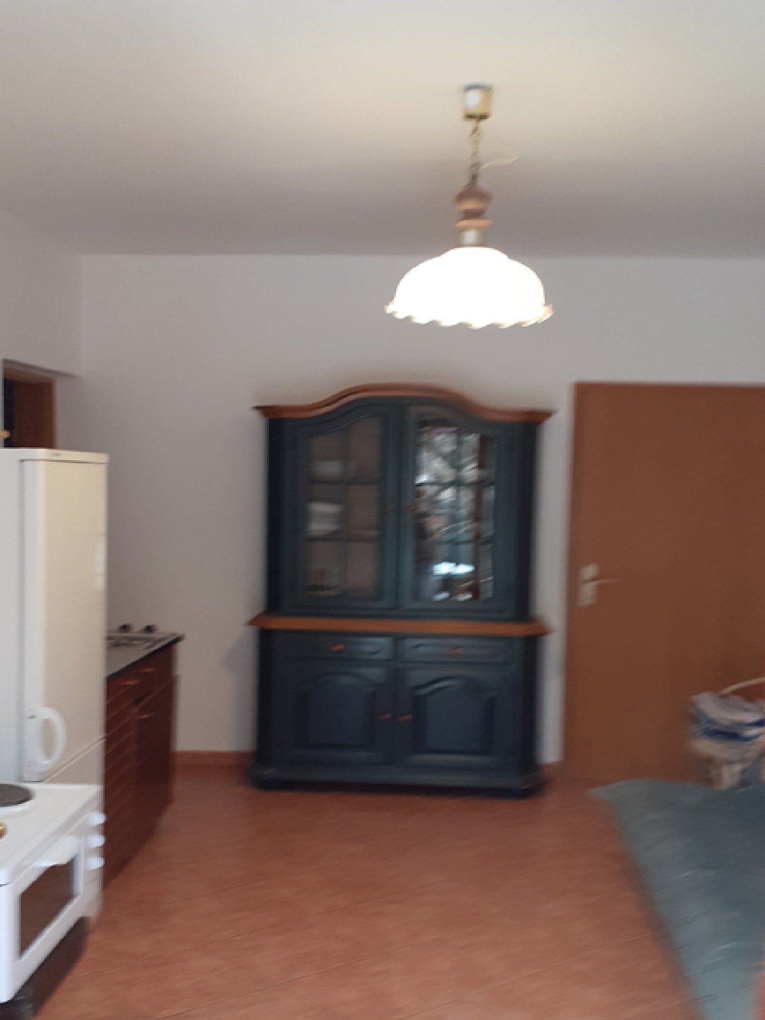 Ein Zimmer mit einem weißen Kühlschrank, einem Holzschrank, einem blauen Sofa und einer Deckenleuchte.