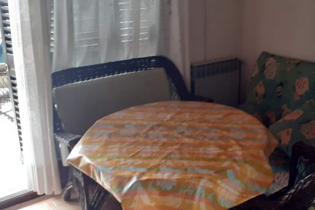 A room with a round table covered by a patterned tablecloth, a chair with a dark frame, and a patterned sofa.