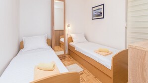 Ein kleines, sauberes Zimmer mit zwei Einzelbetten, einem Holzschrank, einem Spiegel und einem gerahmten Bild an der Wand.