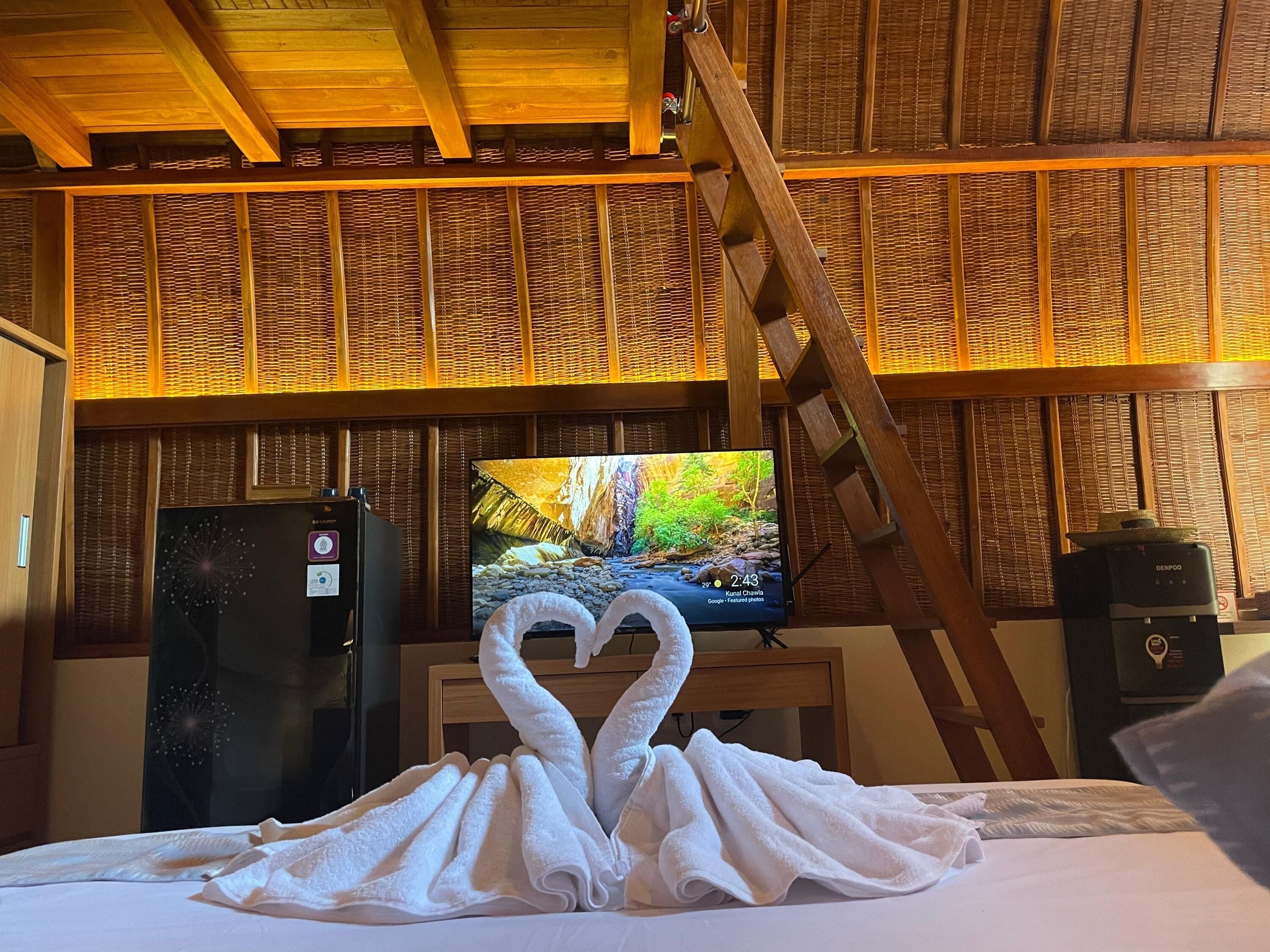 A hotel room with a bed, a TV displaying a scenic image, and a decorative towel arrangement.