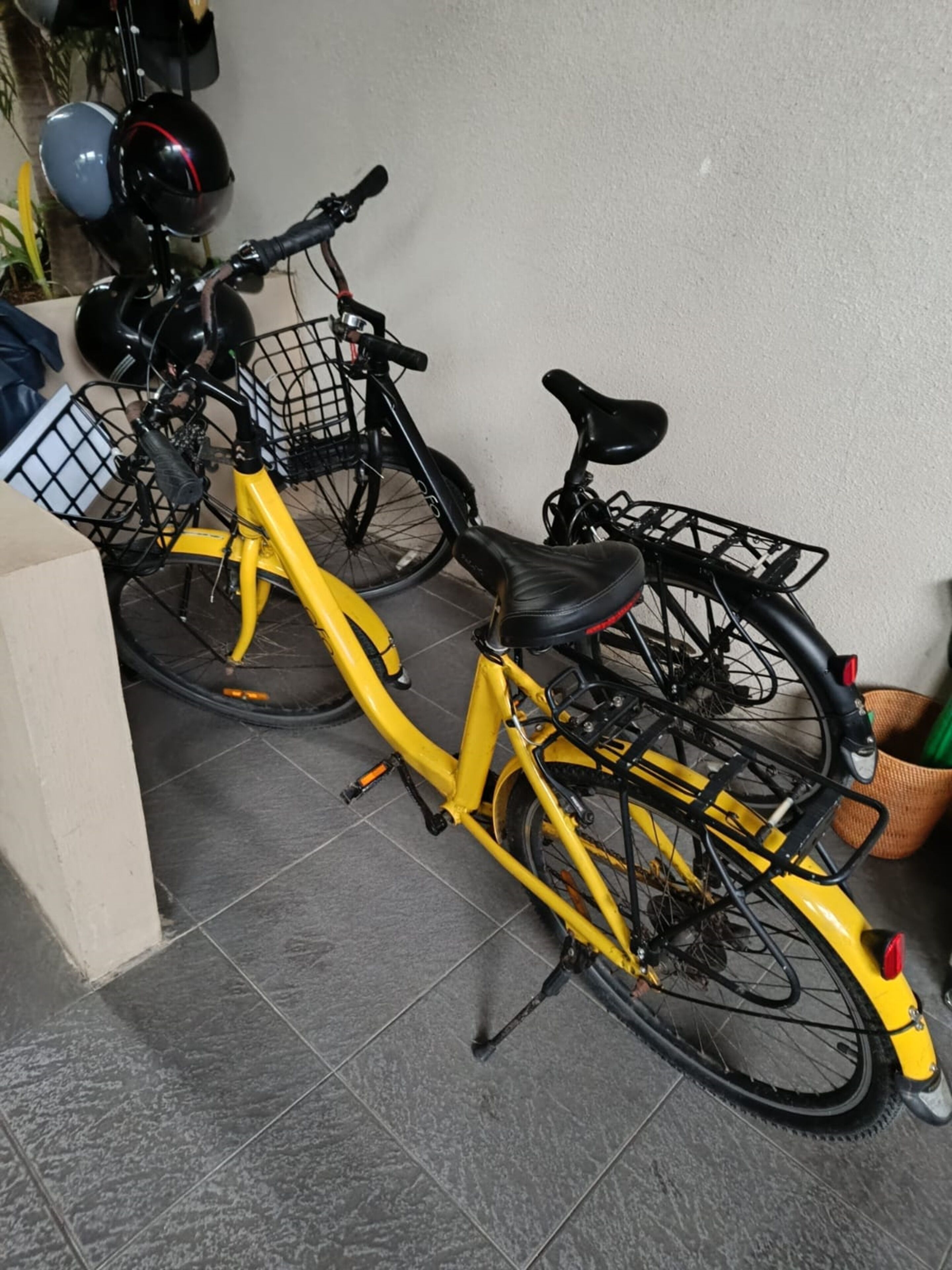 Dos bicicletas estacionadas en el interior, una amarilla y otra negra, con canastas delanteras y traseras.