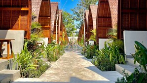 A pathway leading to a row of wooden bungalows with thatched roofs, surrounded by lush greenery. - Abian Klumpu Villa & Spa Sanur Bali (Denpasar)