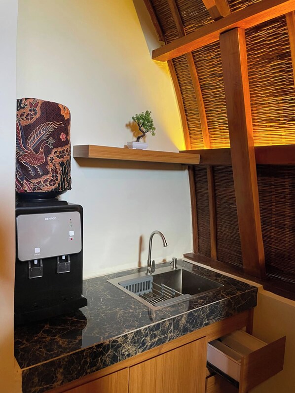 A kitchen with a black marble countertop, a sink, a coffee machine, and a small potted plant on a shelf above the sink.