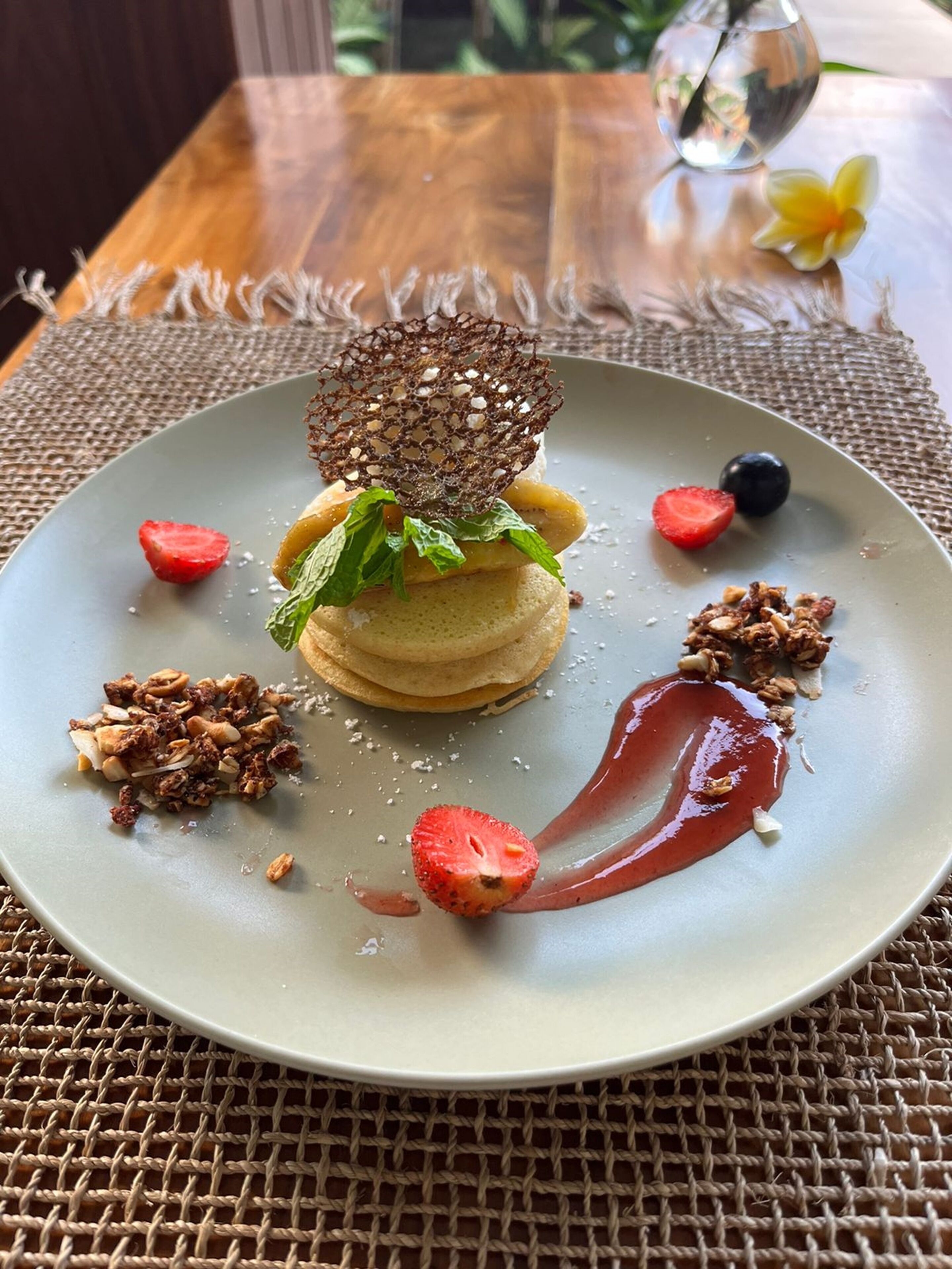 Un plato con panqueques, frutos rojos y un trozo de chocolate sobre un posavasos tejido.