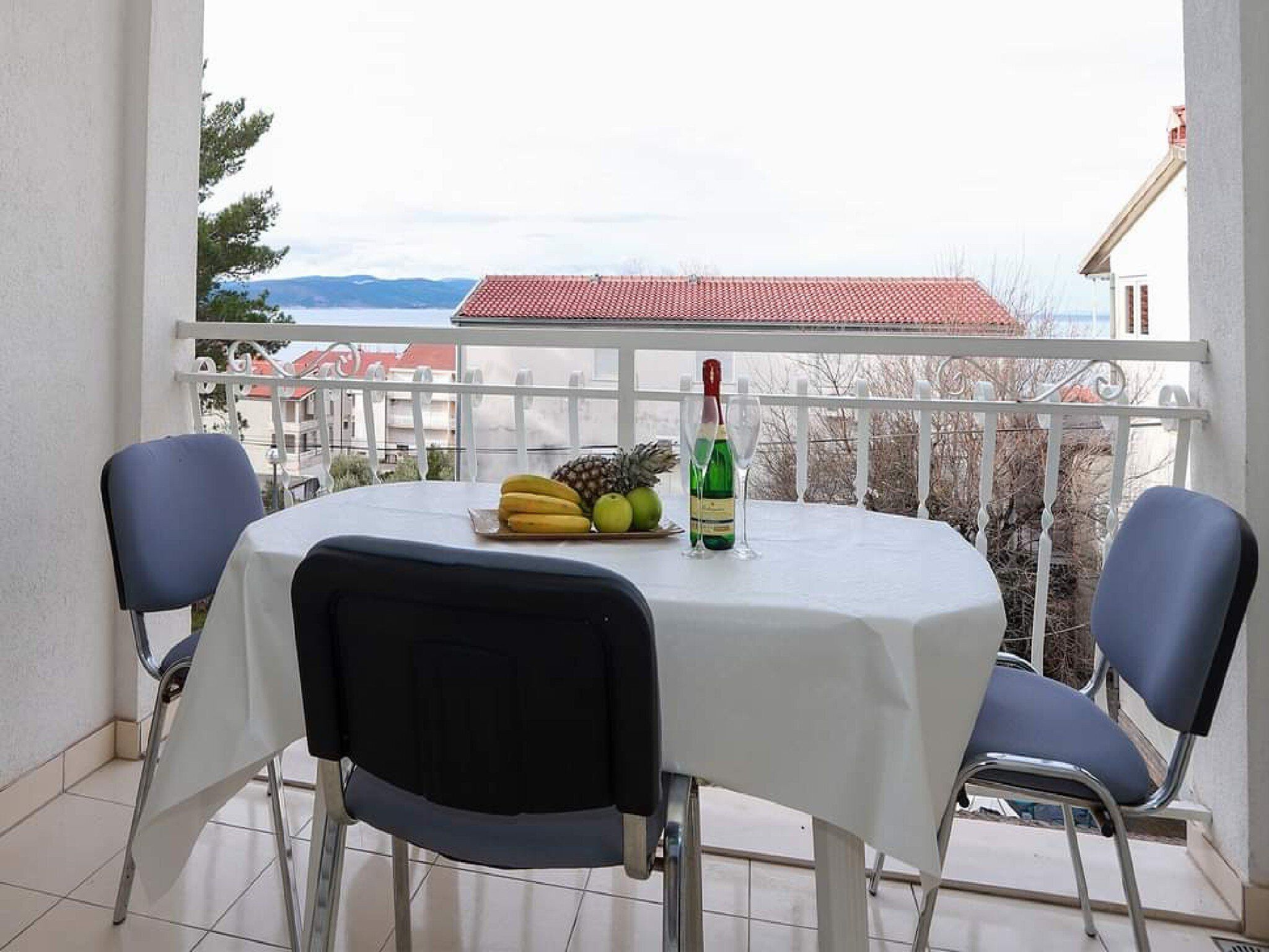 A balcony with a table set for two, featuring a bottle of champagne, a pineapple, and bananas.