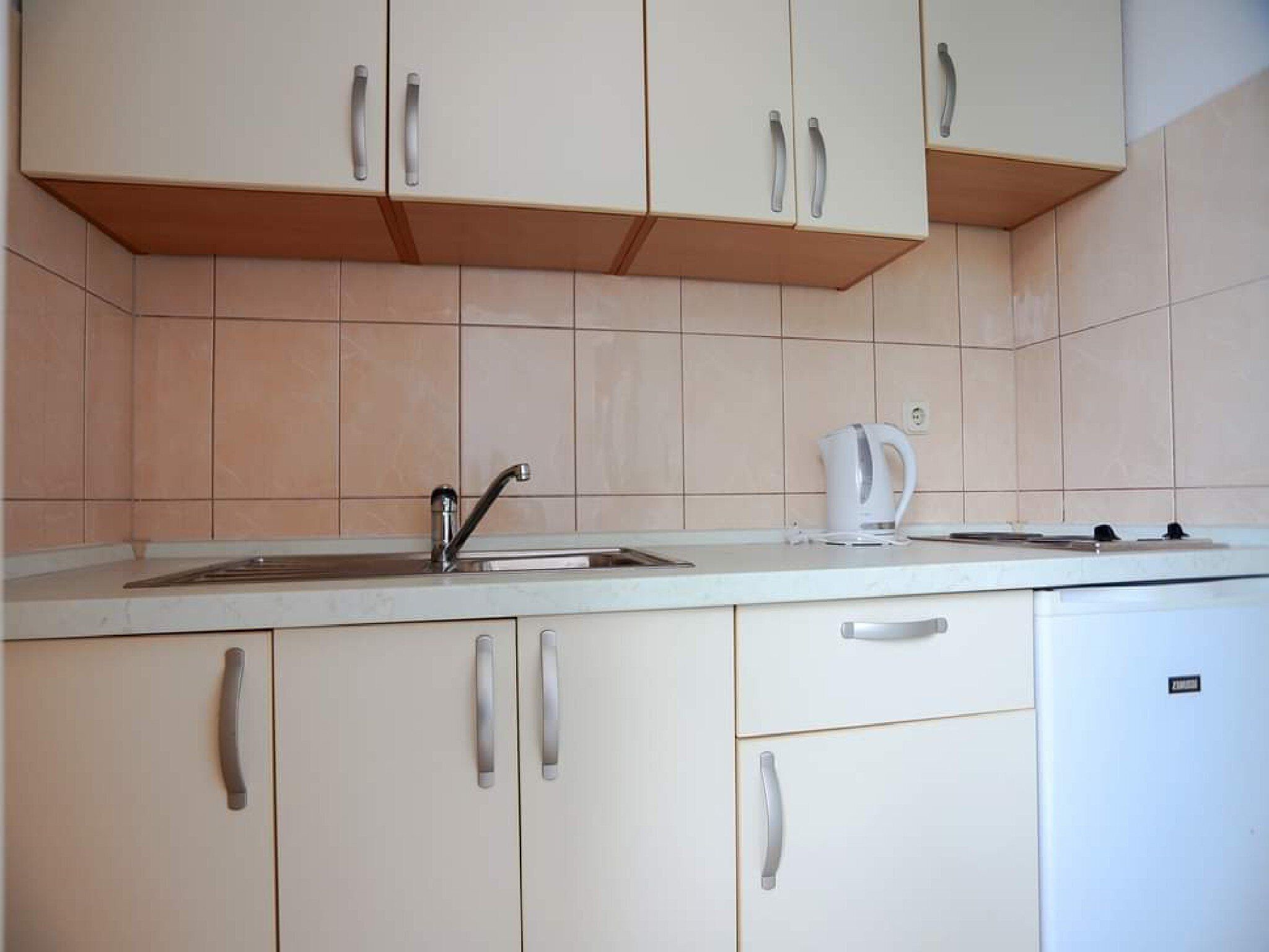 A kitchen with white cabinets, a sink, a kettle, and a stove.