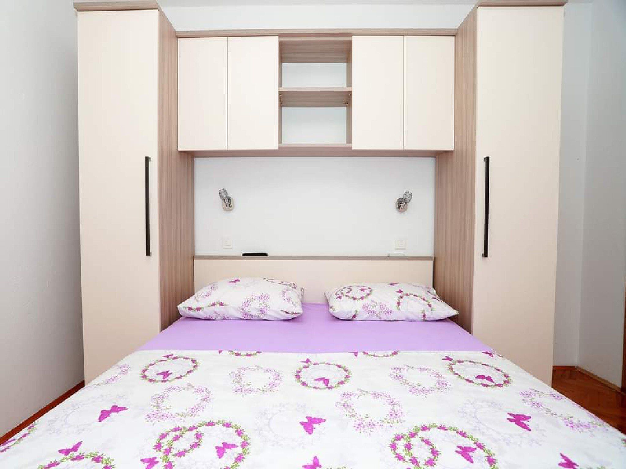 A bedroom with a bed, two pillows, a headboard, and a wardrobe with two doors.