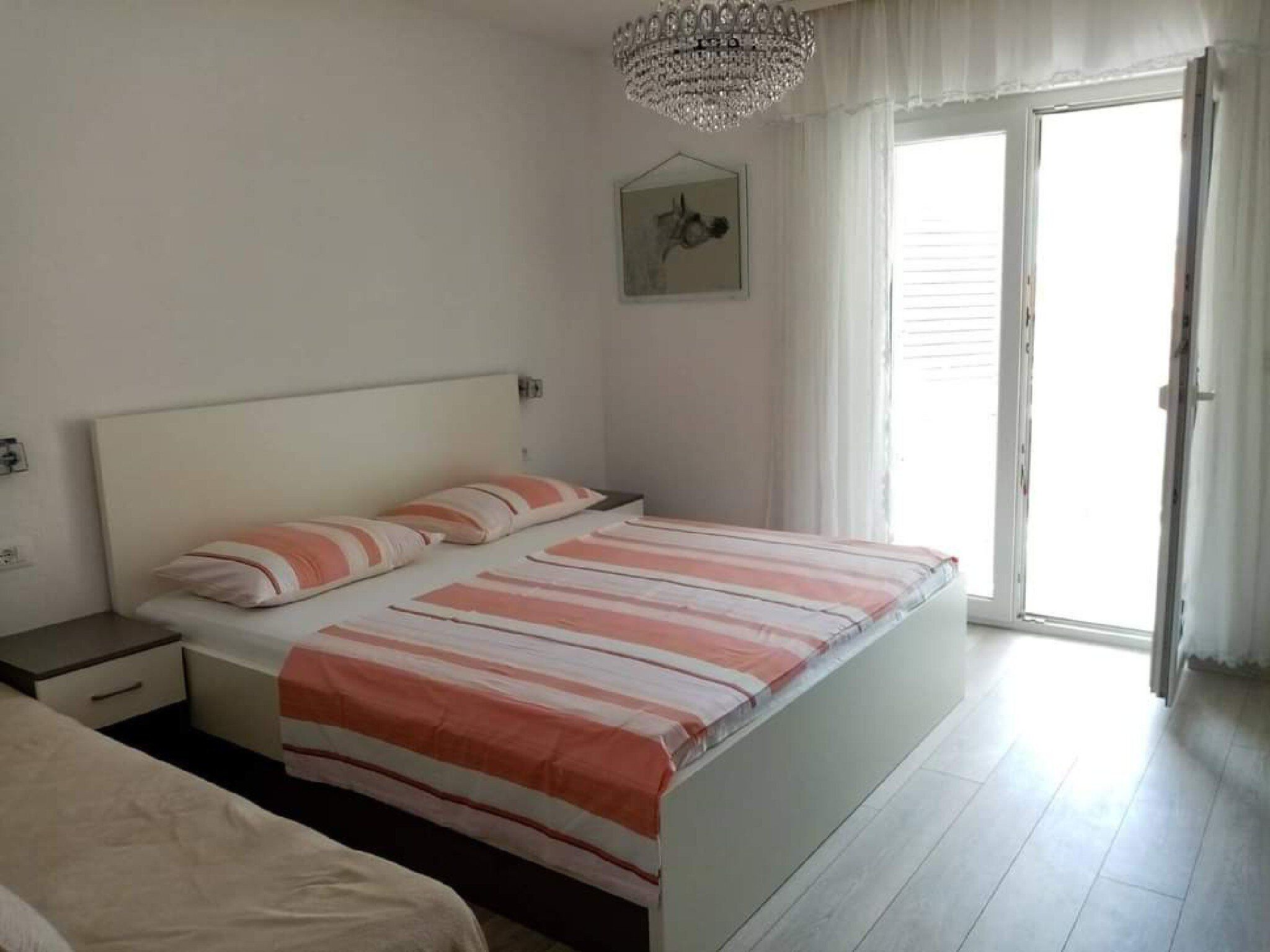 Une chambre à coucher comprenant un lit, une table de chevet, une commode, un lustre et une fenêtre avec des rideaux.