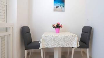 A small dining area with a table, two chairs, a pink flower vase, and a beach scene painting on the wall.