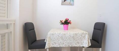 A small dining area with a table, two chairs, a pink flower vase, and a beach scene painting on the wall.