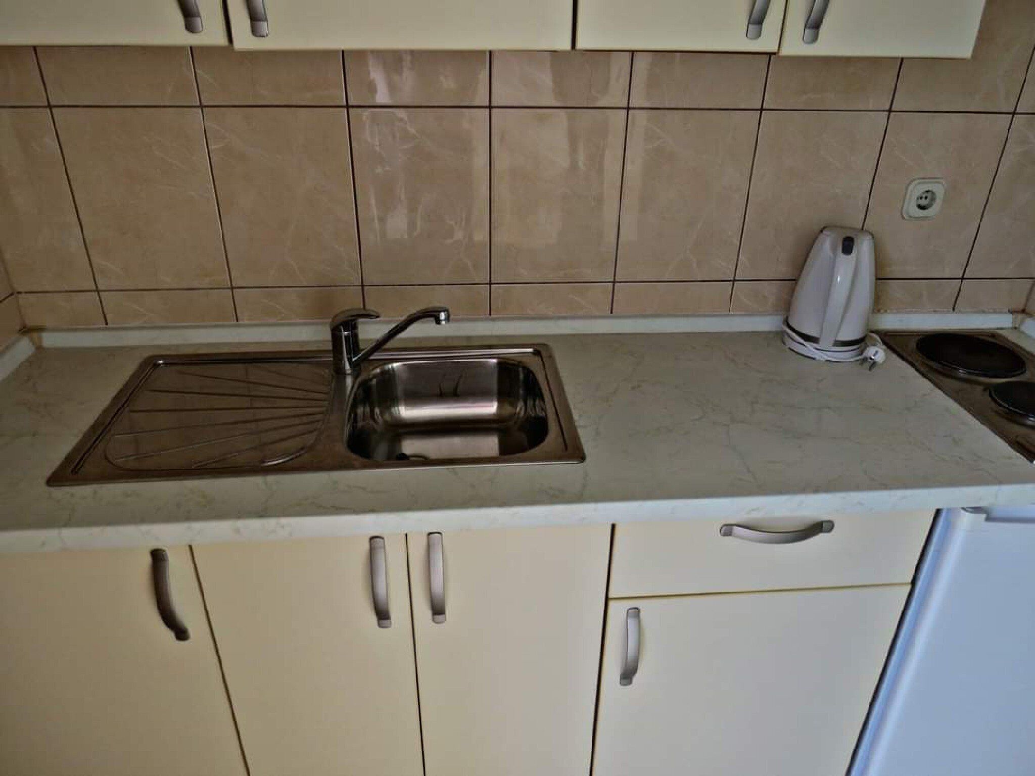 Una cocina con un lavaplatos de acero inoxidable, un hervidor y una estufa.