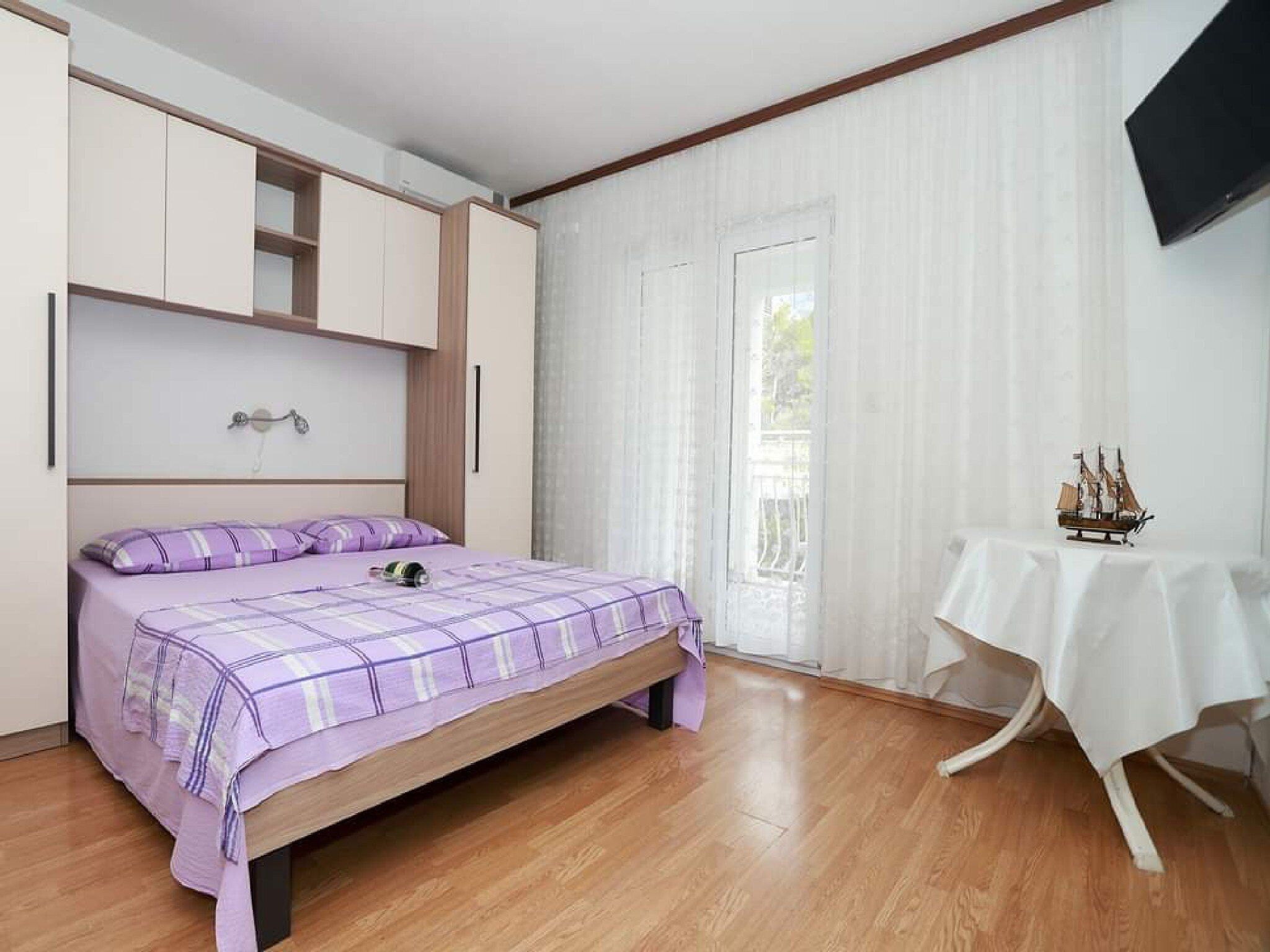 Un dormitorio con cama, un armario, una mesa con un modelo de barco y una puerta con cortinas.