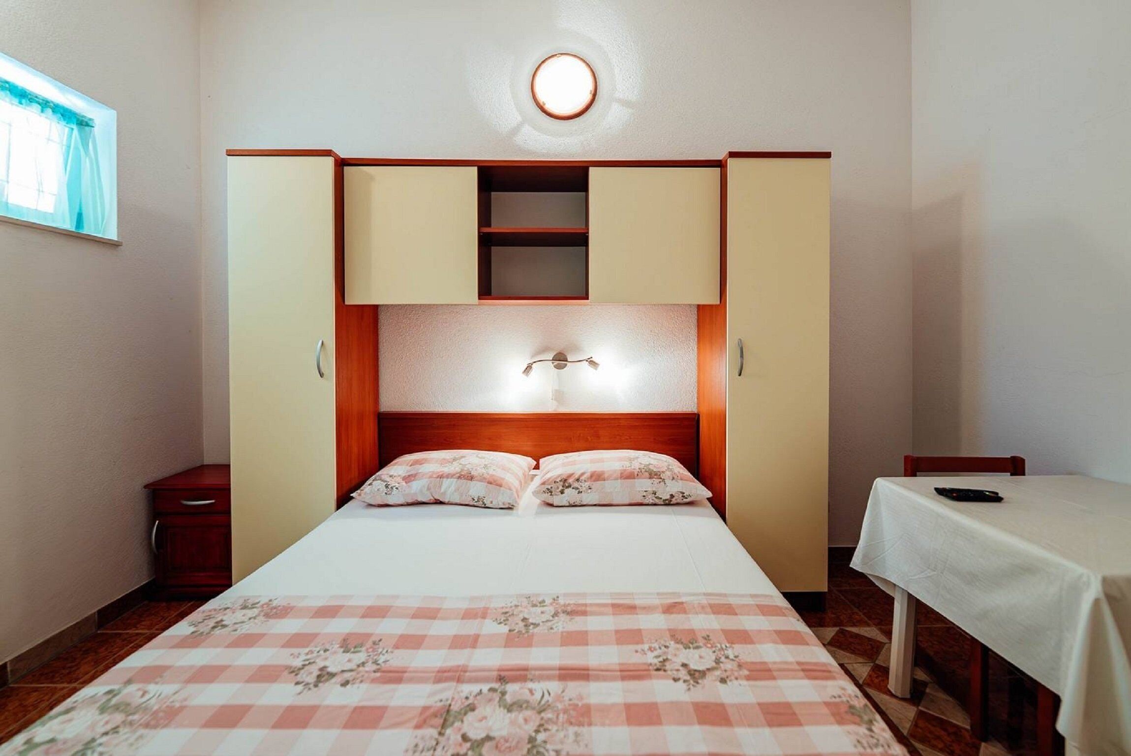 A bedroom with a bed, a nightstand, a wardrobe, and a table with a chair.