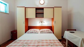 A bedroom with a bed, a nightstand, a wardrobe, and a table with a chair.