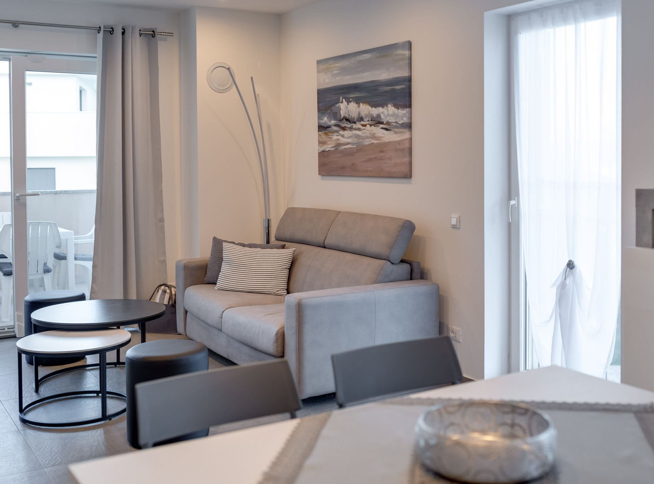 Un salon moderne avec un canapé gris, une table basse ronde et un tableau représentant une scène de plage.