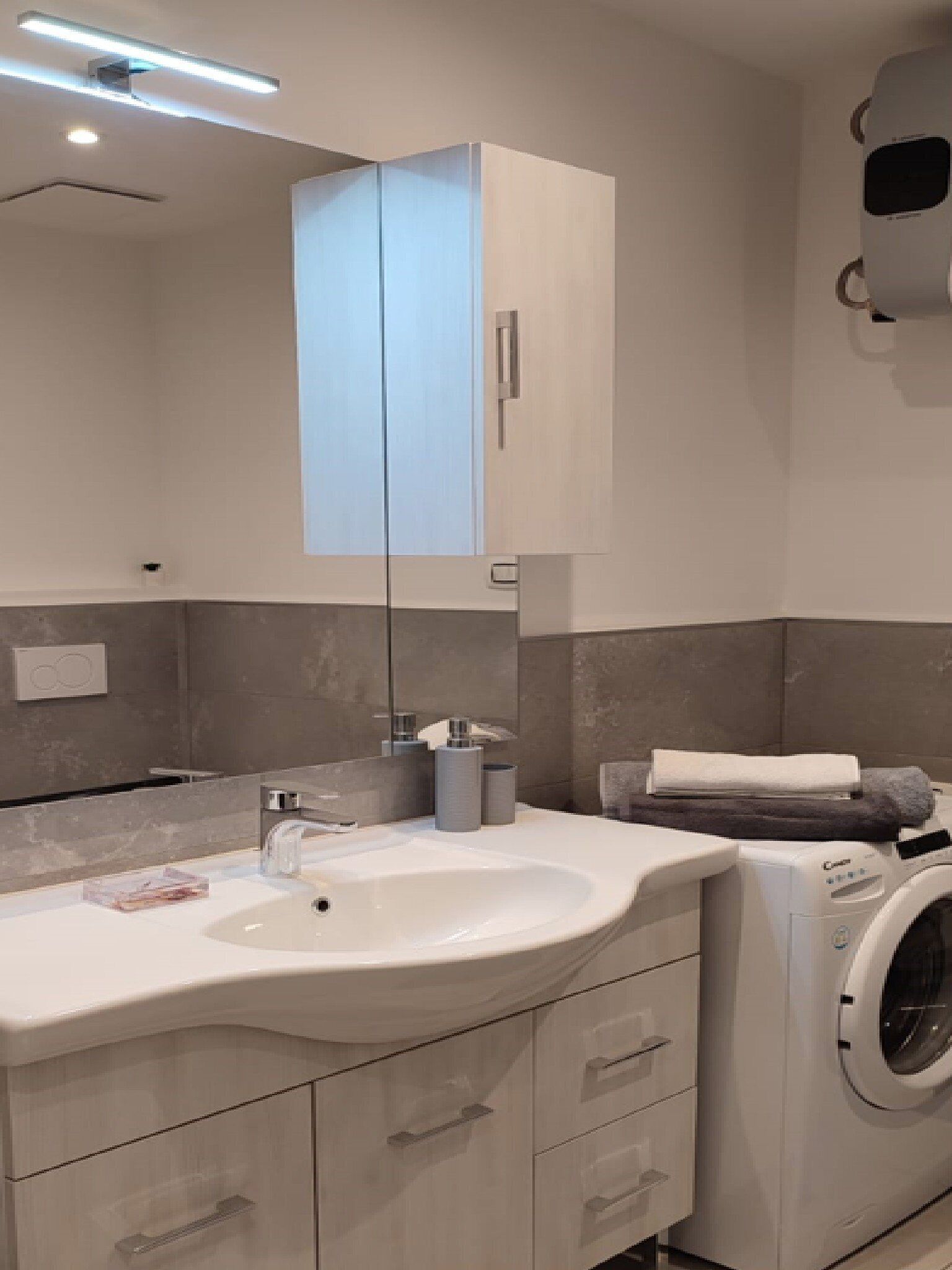 A modern bathroom with a white sink, a built-in washing machine, and a large mirror.
