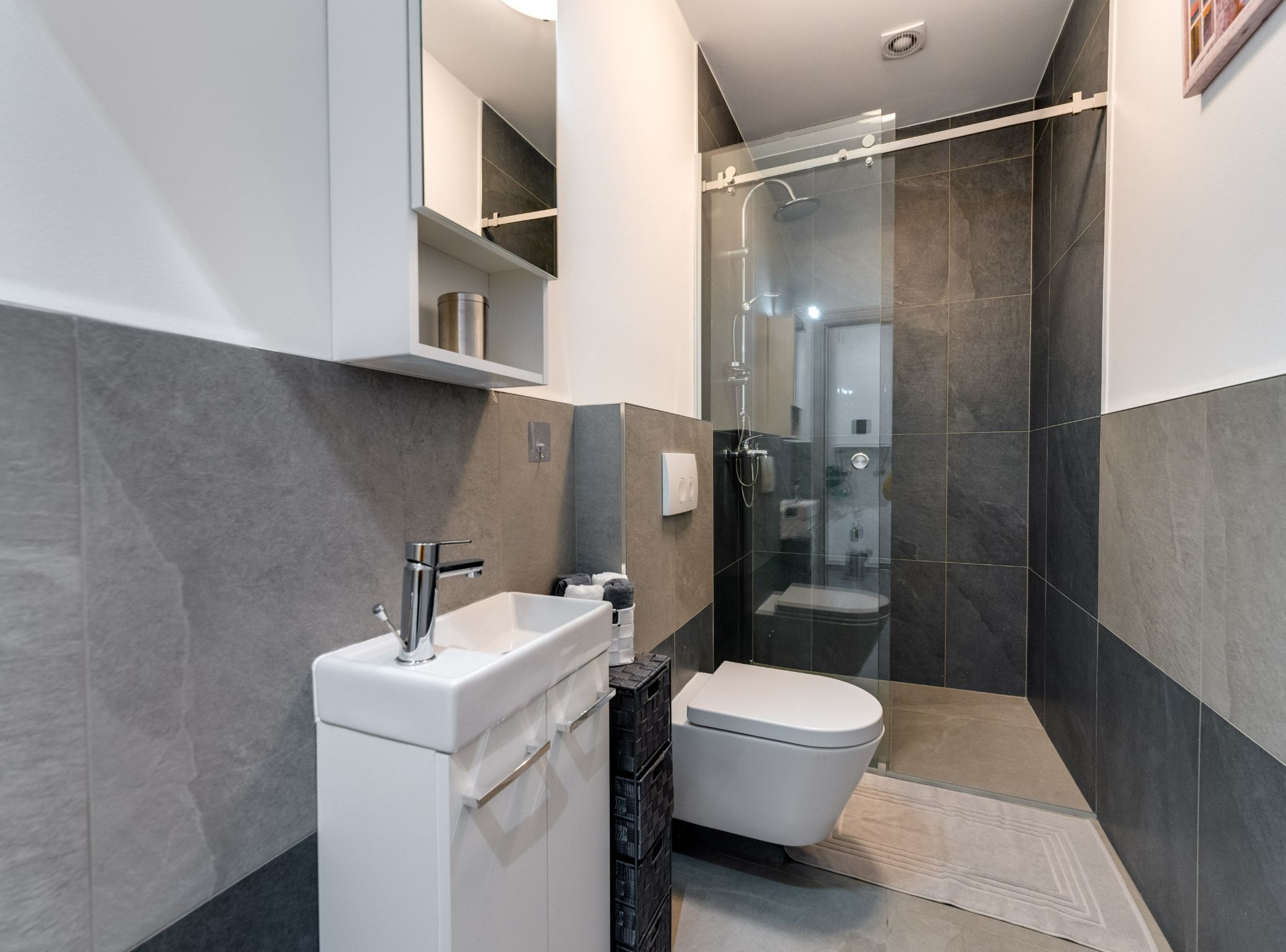 Une salle de bain moderne avec un lavabo blanc, des toilettes et une douche séparée par une paroi de verre.