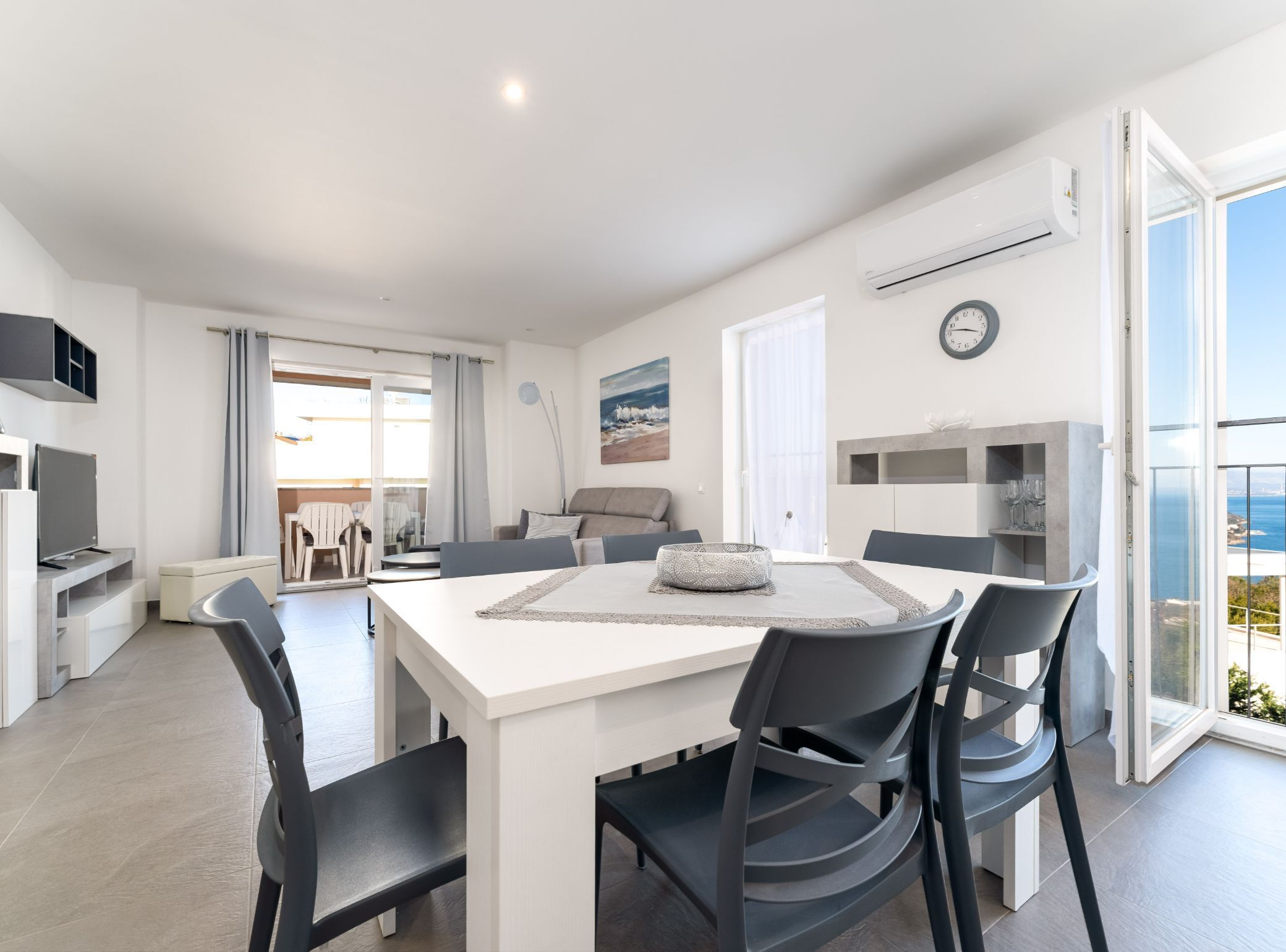 A modern living room with a dining area, a TV, and a view of the sea.
