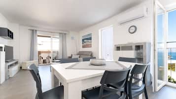 A modern living room with a dining area, a TV, and a view of the sea.