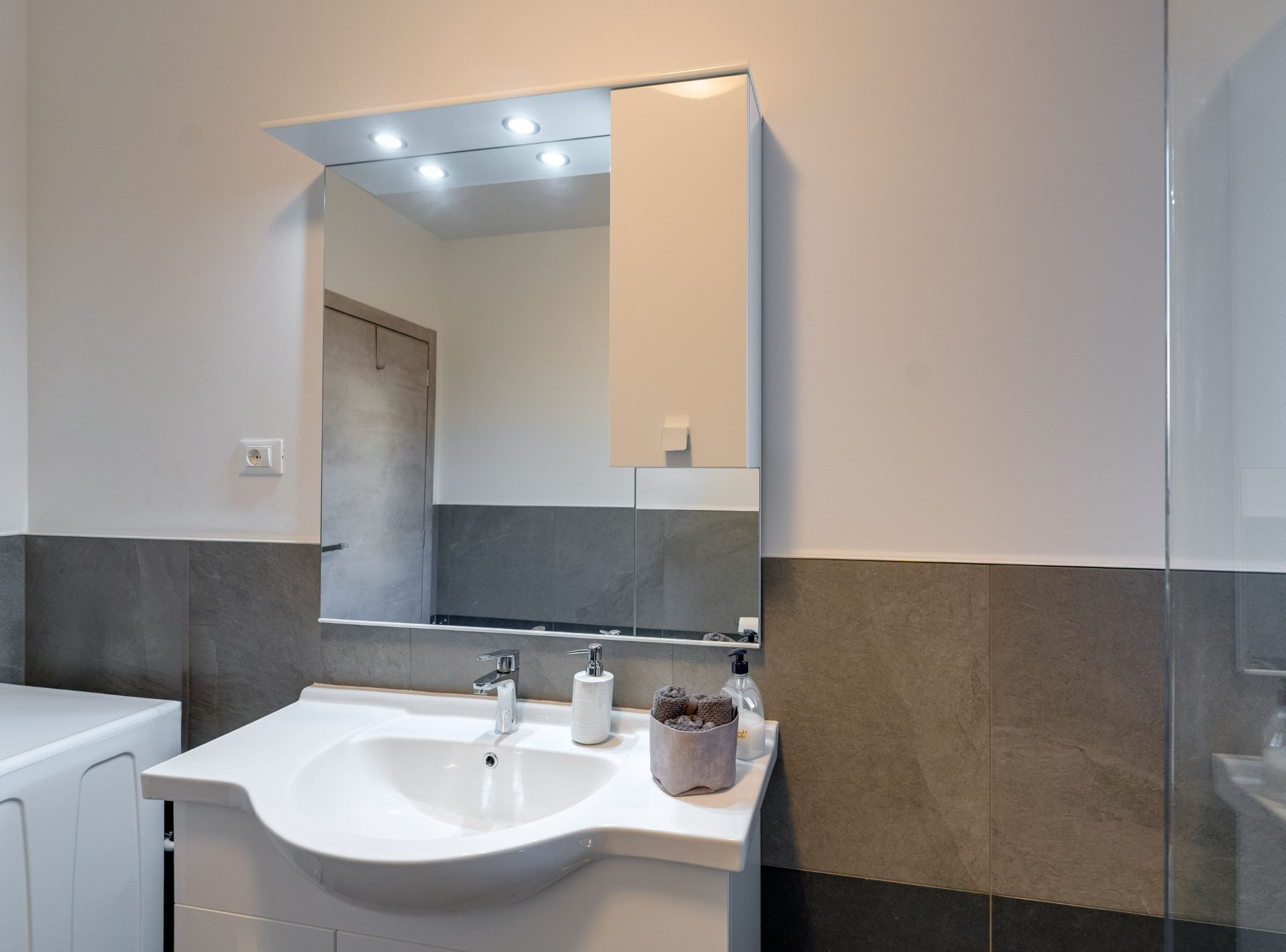 A modern bathroom with a white sink, a large mirror, and a towel holder.