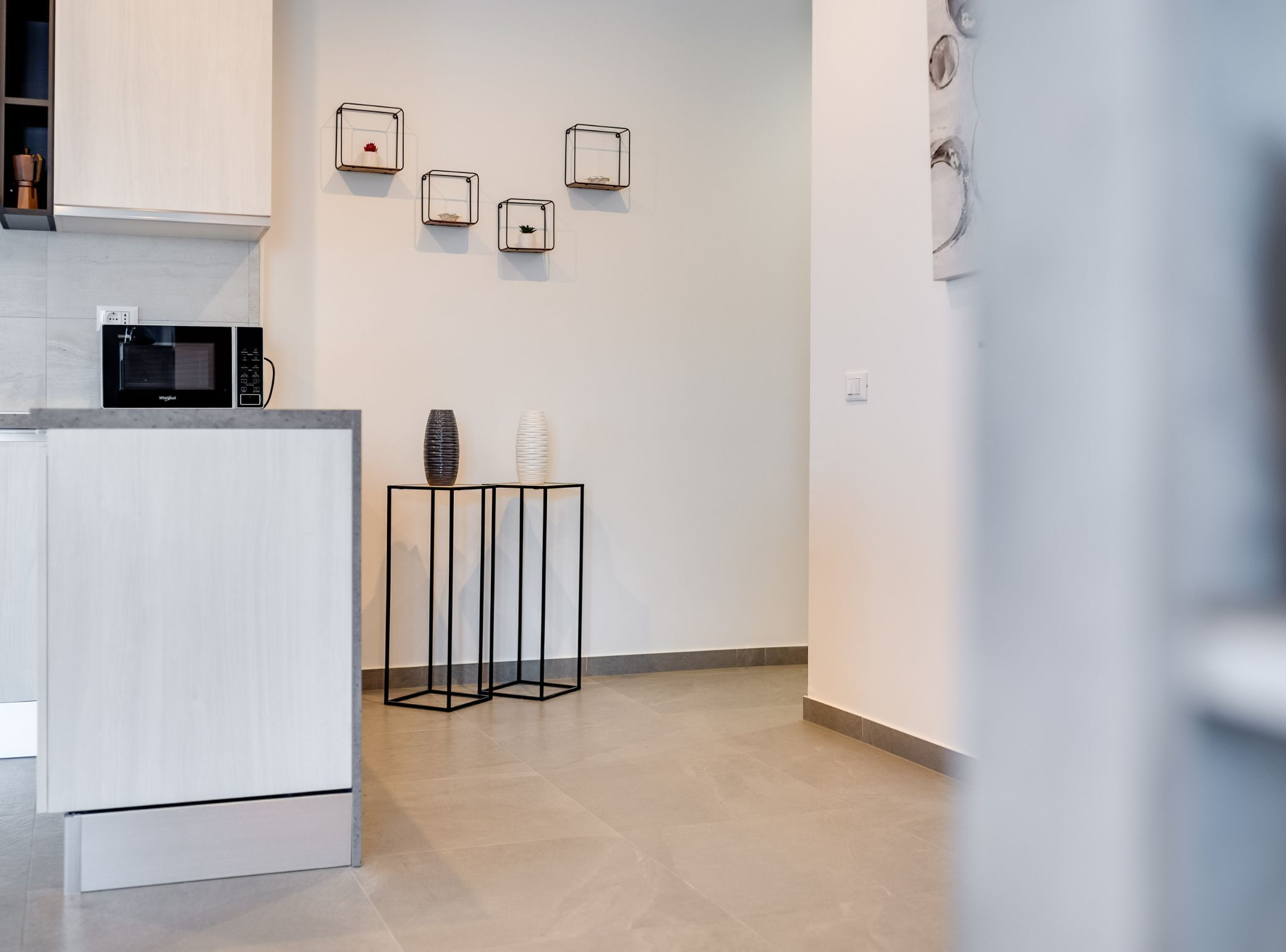 A modern kitchen with a built-in microwave, a white cabinet, and a black metal stand with two vases.