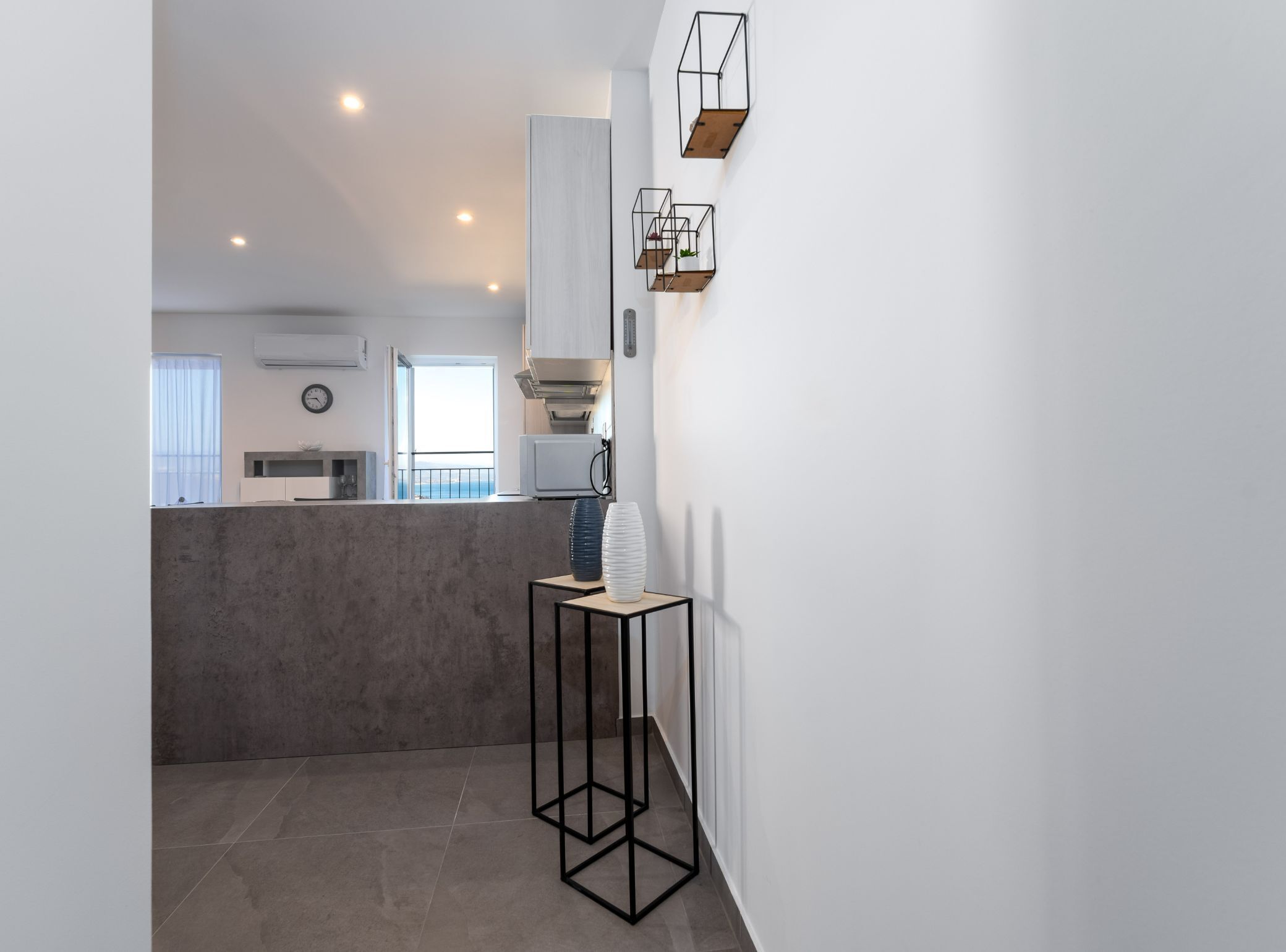 A modern kitchen with a concrete island, white cabinets, and a view to the outside.