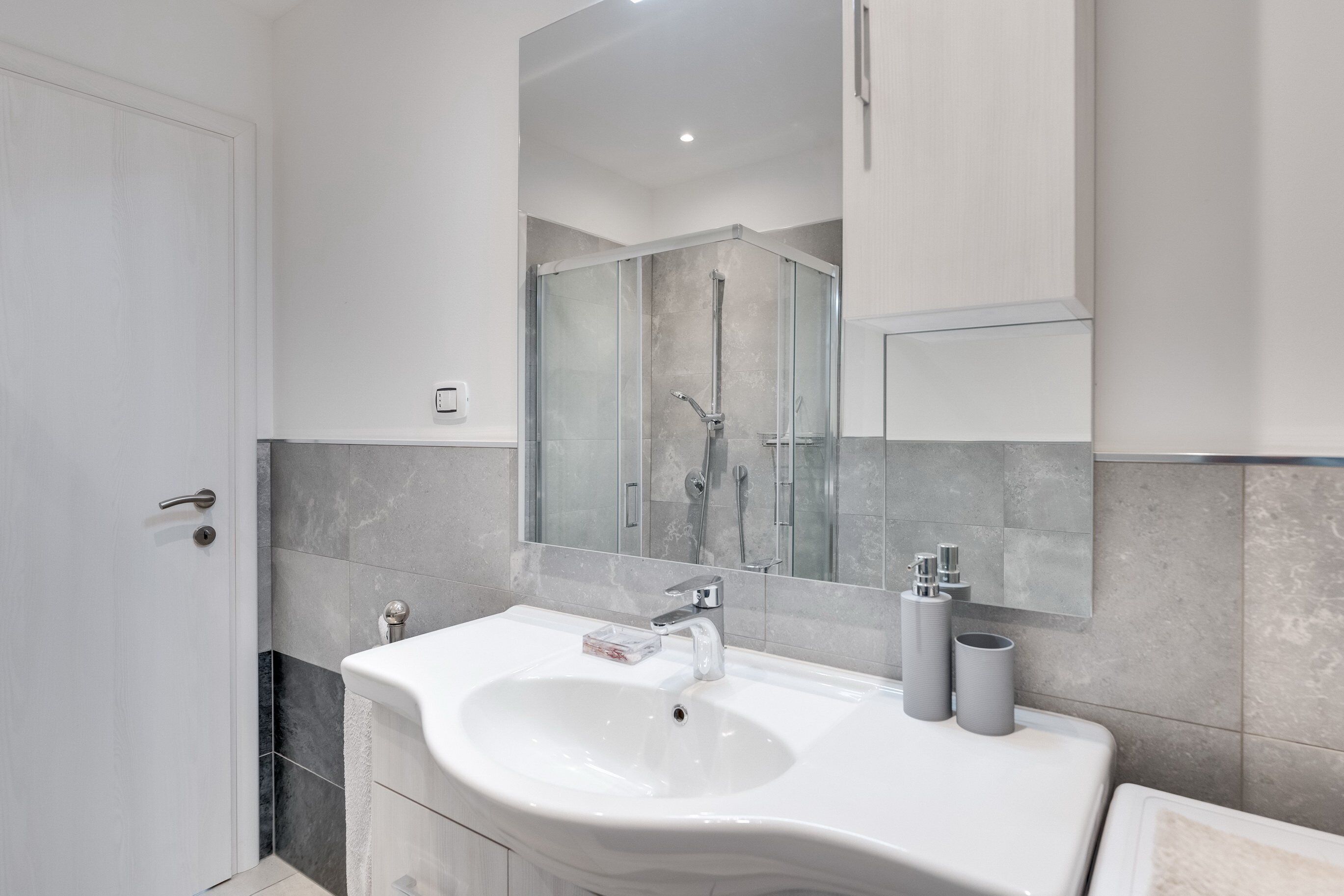Un baño moderno con un lavamanos blanco, un espejo grande y una cabina de ducha.