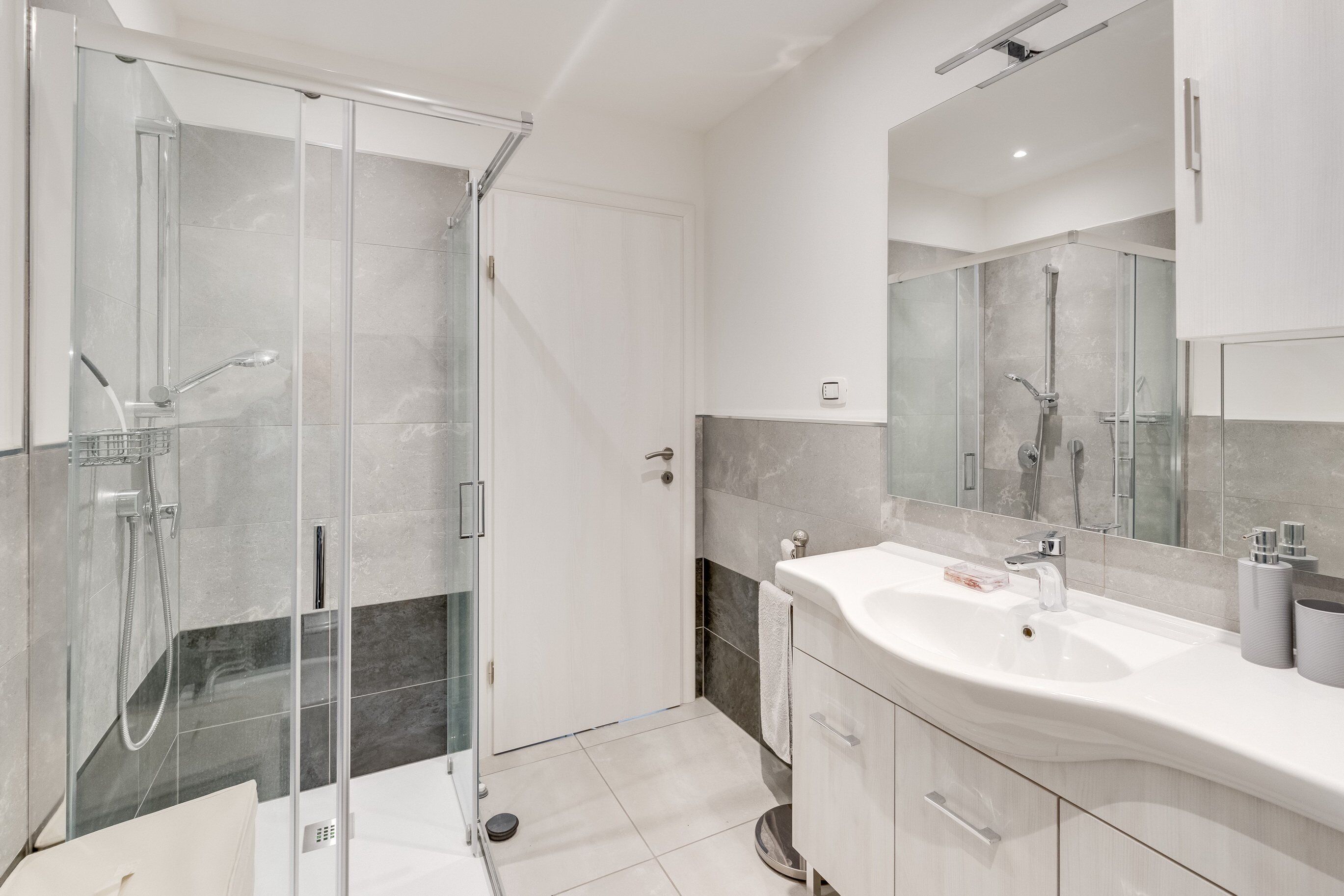 Une salle de bain moderne avec une douche à parois de verre, un grand miroir et un meuble-lavabo blanc.