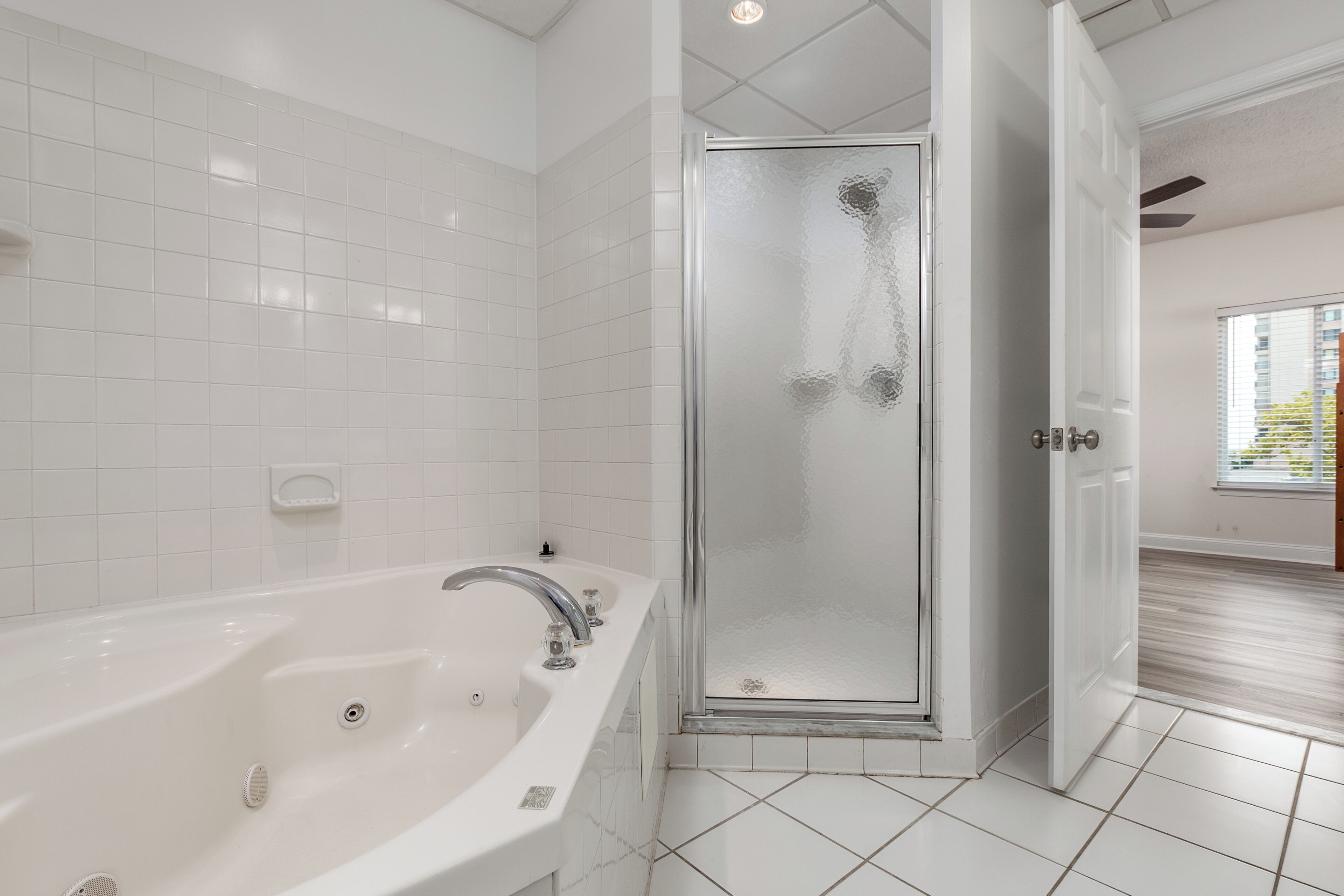 A modern bathroom with a large bathtub, a glass-enclosed shower, and white tiled walls.