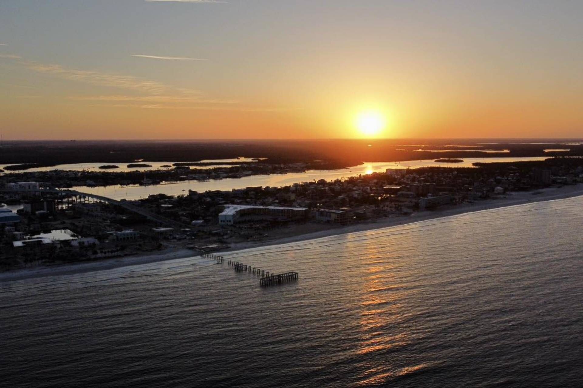A coastal cityscape at sunset with a pier extending into the water.