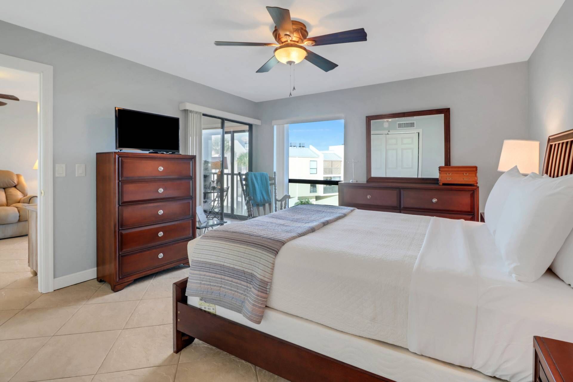 A bedroom with a bed, dresser, TV, and a ceiling fan.
