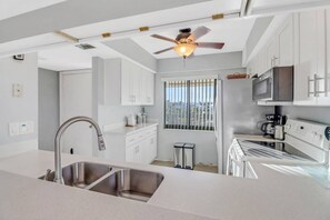 A modern kitchen with a double sink, stainless steel appliances, and a ceiling fan. - Lovely End-Unit, Lagoon-Front Community, South of Mid-Island! Heated Community Pool! Free Parking! (Fort Myers Beach)