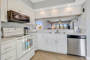 A modern kitchen with white cabinetry, stainless steel appliances, and a view to the outside. - Lovely End-Unit, Lagoon-Front Community, South of Mid-Island! Heated Community Pool! Free Parking! (Fort Myers Beach)