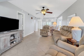 A spacious living room with a flat-screen TV, a ceiling fan, and a large sofa. - Lovely End-Unit, Lagoon-Front Community, South of Mid-Island! Heated Community Pool! Free Parking! (Fort Myers Beach)