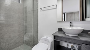 Un baño moderno con cabina de ducha de vidrio, inodoro blanco y un lavamanos grande con espejo arriba.