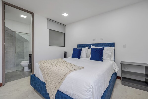 Un dormitorio con cama, mesita de noche, espejo y baño completo.