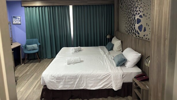 Een hotelkamer met een groot bed, een bureau, een stoel en een decoratief wandpaneel.