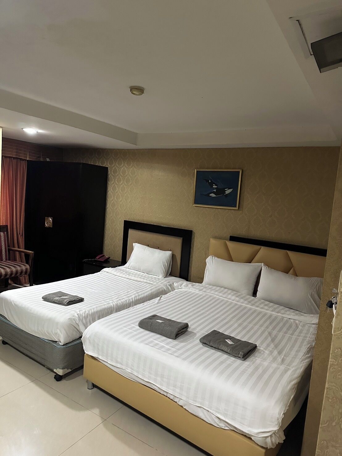 A hotel room with two beds, a headboard, a nightstand, a chair, and a painting on the wall.