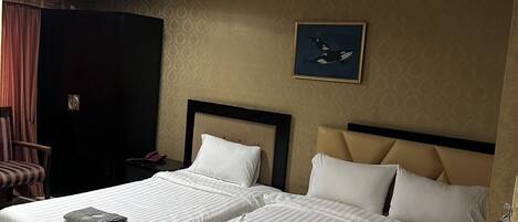 A hotel room with two beds, a headboard, a nightstand, a chair, and a painting on the wall.