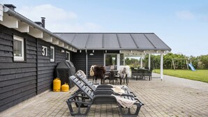 En terrasse med liggestole, et overdækket bord og en grill.