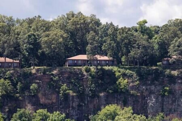 A row of buildings on a cliff with dense forest in the background.